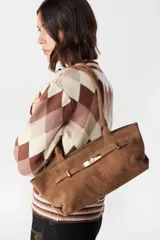 Cartera tipo baguette de cuero gamuzado color marrón, con diseño alargado y cierre frontal mediante una tira con hebilla metálica dorada. Cuenta con doble asa de hombro.