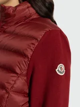 Cardigan híbrido de Moncler con frente acolchado tipo puffer en color bordó y mangas de punto de lana virgen al tono. Presenta cierre frontal completo y cuello alto.