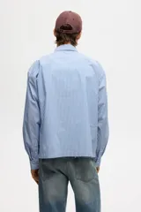 Camisa de corte relajado confeccionada en tejido de algodón con estampado de rayas verticales. Presenta cuello americano, cierre frontal con botones, un bolsillo en el pecho y mangas largas con puños abotonados.