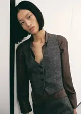 Chaleco de lana jaspeado en color gris, con cuello en V, tirantes anchos, dos bolsillos de ribete frontales y cierre delantero con botones.