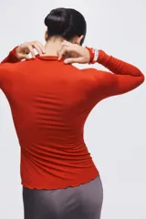 Top de punto color rojo con cuello alto y mangas largas. Presenta un diseño liso con terminaciones de borde sobrehilado en los puños y en el ruedo.