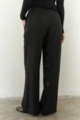 Pantalón negro de corte amplio con cintura alta, cierre de cremallera y botón. Cuenta con bolsillos laterales y tela bordada.