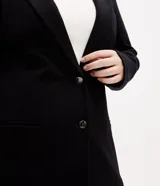 Blazer negro de corte slim alargado, confeccionado en punto roma con abotonado doble frontal, solapas de muesca y bolsillos de ojal en los laterales.