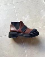 Botas tipo chelsea de cuero vacuno en combinación de colores marrón y negro, con suela track dentada y elásticos laterales.