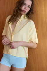 Camisa de corte fluido con cuello solapa y manga corta con dobladillo. Presenta cierre frontal con botones ocultos bajo una tapeta.