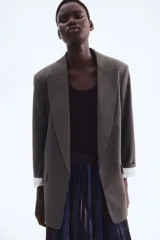 Blazer de sarga con diseño a cuadros, solapas de pico y frente abierto. Cuenta con bolsillos delanteros ribeteados con solapa y mangas diseñadas para ser remangadas, revelando un forro a rayas. Prenda completamente forrada.