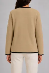 Saco de punto color beige con ribetes en contraste color negro. Presenta un diseño de escote en V, cierre frontal cruzado con botones y dos bolsillos delanteros aplicados.