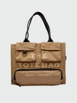 Bolso tipo tote Marc Jacobs modelo The Cargo Canvas Large Tote Bag, color tostado, confeccionado en lona con múltiples bolsillos delanteros con solapa y cierre, detalle de anilla metálica y estampado gráfico con el nombre de la marca. Cuenta con asas dobles para el hombro.