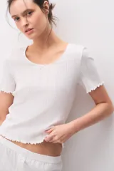 Remera de algodón blanca de manga corta, con diseño texturado, escote redondo y pequeño lazo decorativo en el centro. Presenta terminaciones con ondas en cuello, mangas y ruedo.