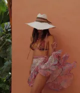 Falda playera larga estilo pareo, confeccionada en gasa estampada con diseño de algas marinas en tonos rosa, celeste, verde y blanco. Presenta cinturón anudado en la cintura y volantes en la abertura y el bajo.