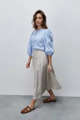 Falda midi color beige de tiro alto y silueta amplia, confeccionada en tela liviana con pinzas en el frente, pasacintos y bolsillos laterales.