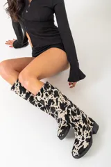 Botas de caña alta con estampado de vaca en blanco y negro, con tacón bajo y puntera redondeada.