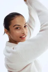 Buzo de punto suave color beige claro, con cuello redondo y abertura frontal con botones dorados. Presenta hombros caídos y puños y bajo acanalados.