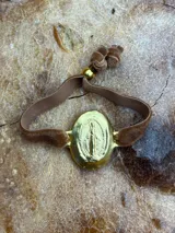 Pulsera elástica de terciopelo marrón con medalla ovalada dorada de la Virgen María.