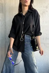 Camisa negra de corte oversize, con cuello clásico, manga larga y bolsillo en el pecho.