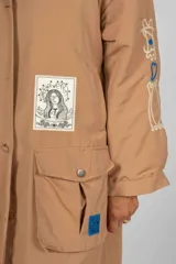 Trench color camel con cuello clásico, solapas grandes, cierre cruzado con botones, cinturón ajustable, bolsillos laterales y largo midi.