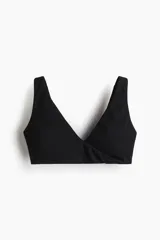 Top de yoga negro confeccionado en tejido funcional con tecnología SoftMove y Lycra Sport. Presenta un diseño con breteles anchos, escote en V y un detalle cruzado o girado en la parte delantera. Incluye copas con relleno extraíble y ofrece sujeción suave para ejercicios de bajo impacto.