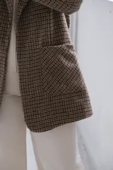 Blazer de corte recto con estampado de cuadros tipo príncipe de gales en tonos marrones y beige. Presenta solapas clásicas, bolsillos frontales aplicados y mangas largas.