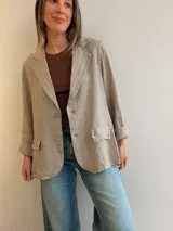 Blazer de lino color beige, de corte relajado y líneas clásicas. Presenta cuello con solapas, cierre frontal con dos botones y bolsillos con solapa en el frente.