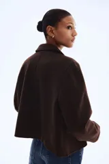 Campera corta de color marrón oscuro con cuello camisero, cierre frontal mediante botones y dos bolsillos delanteros con solapa. Presenta un diseño forrado y corte recto.