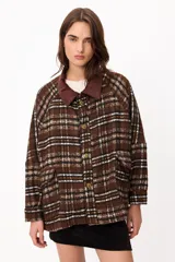 Chaqueta de corte holgado con estampado de cuadros en tonos marrones, blancos y negros. Presenta cuello de pana en color marrón oscuro, cierre frontal con botones metálicos y bolsillos laterales amplios.