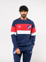 Buzo de cuello redondo confeccionado en felpa, con diseño de bloques de color en azul, rojo y blanco. Presenta el logo de Umbro y el escudo del Club Nacional de Football bordados en el frente.