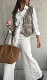 Chaleco de gamuza en color verde oliva, con diseño de bordados florales en hilo blanco y detalles de tachas metálicas. Presenta un corte clásico con cierre frontal de botones.