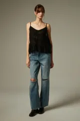 Musculosa negra de breteles finos, confeccionada en algodón con diseño plisado y detalles de encaje. Presenta un corte holgado con volados en el ruedo y escote profundo.