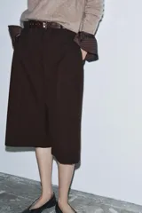 Bermuda larga color marrón oscuro, de tiro medio con cintura con trabillas. Presenta bolsillos laterales ocultos en la costura y detalle de raya planchada. Cierre frontal con cremallera, botón y ganchos metálicos.