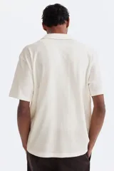 Camisa de manga corta color blanco hueso, de punto jacquard en mezcla de algodón, con cuello abierto y cierre frontal de botones.