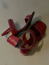 Sandalias de cuero rojo con taco medio, punta cuadrada y tiras superiores trenzadas. Cuentan con tira ajustable al tobillo mediante hebilla metálica.