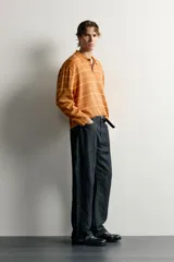 Polo de punto de algodón con diseño a rayas horizontales en tonos tostado y amarillo, cuello solapa y cierre frontal parcial con tres botones. Presenta mangas largas y efecto lavado.