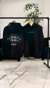 Canguro oversize negro con capucha y bolsillo tipo canguro. Presenta el texto "TOP STYLE COLLECTIONS" en el pecho y un estampado gráfico en la espalda con óvalos y texto en tonos celestes y blancos.