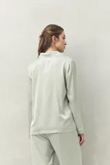 Camisa de pijama color verde menta, de silueta clásica y tacto sedoso. Confeccionada en tejido satinado con leve elasticidad, presenta cuello camisero, cierre frontal con botones y detalles de vivo blanco que realzan el diseño.