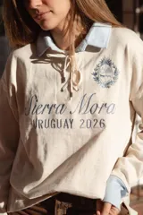 Buzo azul marino de calce relajado, con cuello polo y puños en contraste color crudo, cierre frontal con cordones ajustables y bordados alusivos en el frente.