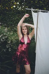 Vestido corto negro con escote en V profundo, estilo halter con tiras para atar al cuello. Presenta un diseño ajustado en el busto con tiras ajustables bajo el mismo que se cruzan y anudan en la espalda, y falda con volado en el ruedo con detalle de encaje.