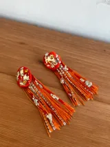Caravanas artesanales con base superior de resina en color marrón con detalles de lámina dorada y cristales incrustados. Presentan flecos largos de hilo marrón combinados con tiras de strass brillante.