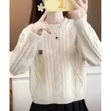 Sweater de punto color crema con diseño de trenzas y rombos, cuello redondo y mangas largas. Presenta un pequeño aplique decorativo en el pecho.