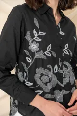 Camisa blanca de algodón con bordado floral en hilo negro en el frente. Camisa de corte clásico, con cuello abotonado, mangas largas con puños abotonados y cierre frontal con botones.