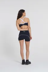 Top deportivo negro con tirantes blancos regulables, escote medio y compresión media.