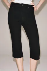 Jeans capri negro de tiro medio, corte recto y diseño de cinco bolsillos. Cuenta con trabillas en la cintura y cierre frontal con cremallera y botón metálico.