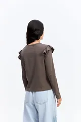 Remera de manga larga color marrón, con cuello redondo y detalle de volados en los hombros. Posee un corte ajustado al cuerpo.