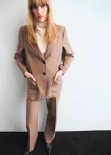 Chaqueta de traje color tostado con cuello de solapa, cierre frontal de dos botones, mangas largas y bolsillos de parche delanteros. Cuenta con forro interior y diseño recto.