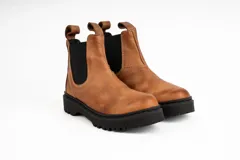 Bota tipo Chelsea de cuero color marrón, con paneles elásticos laterales en color negro, costuras a la vista y suela de goma dentada negra.