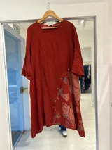 Vestido midi terracota de lino, con diseño asimétrico cruzado en el frente, decorado con botones y un inserto de tela con estampado floral en tonos rosados y marrones en la parte inferior.