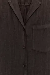Camisa de lino color negro, de manga larga, con cuello solapa y cierre frontal con botones. Presenta un bolsillo de parche en el delantero.