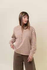 Buzo liviano de manga larga con diseño de rayas horizontales en color beige y blanco. Presenta un cuello redondo con cartera frontal de botones tipo henley, hombros caídos y calce holgado con puños acanalados.