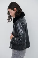 Chaqueta de efecto cuero brillante con acabado charol, cuello con solapas de piel sintética, cierre frontal con botones y bolsillos laterales.