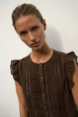 Blusa de cuello redondo y manga sisa con volantes, color marrón, con detalles de entredoses a tono, jaretas delanteras y cierre frontal con botones.