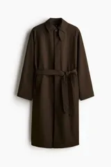 Gabardina estilo Mac de color marrón oscuro, confeccionada en sarga suave. Presenta cuello clásico, cierre frontal con botones ocultos, manga raglán con trabilla y botón en los puños, bolsillos insertados y cinturón extraíble para atar a la cintura. Tiene una abertura en la espalda y forro interior.